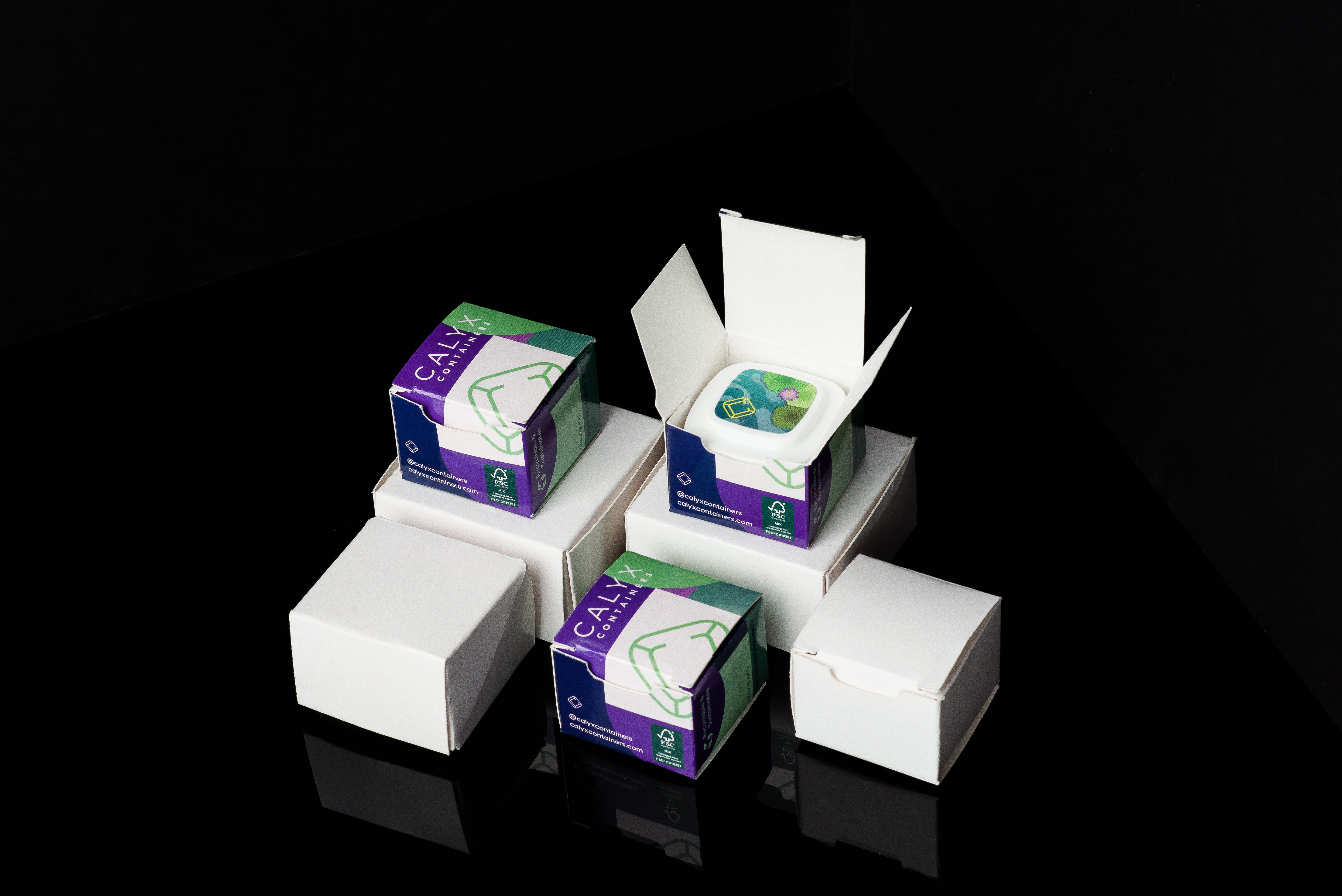 A stack of white boxes and custom-printed corrugated boxes with green and purple labels on a black background