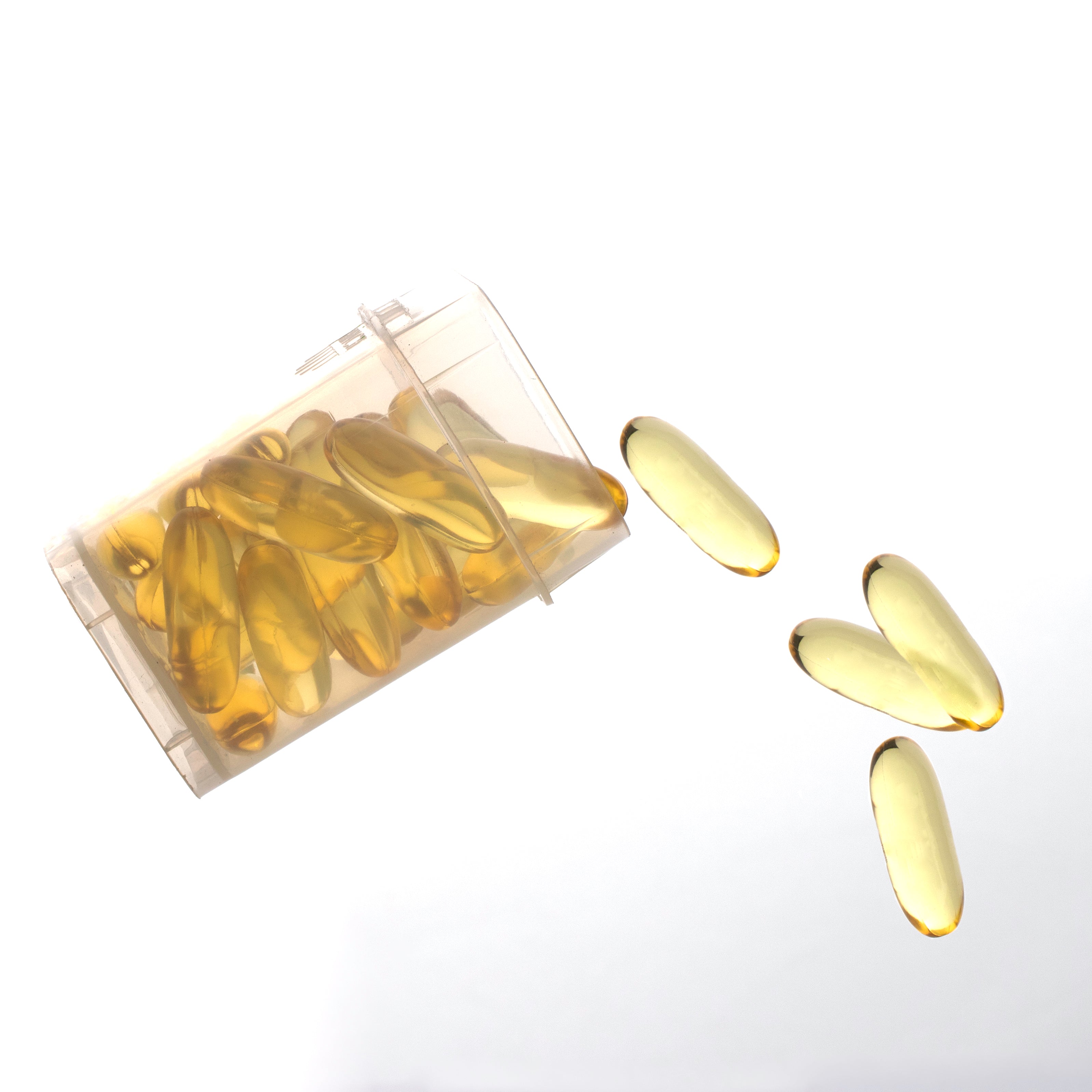 Yellow capsules spilling out of a transparent plastic packaging container on a white background
