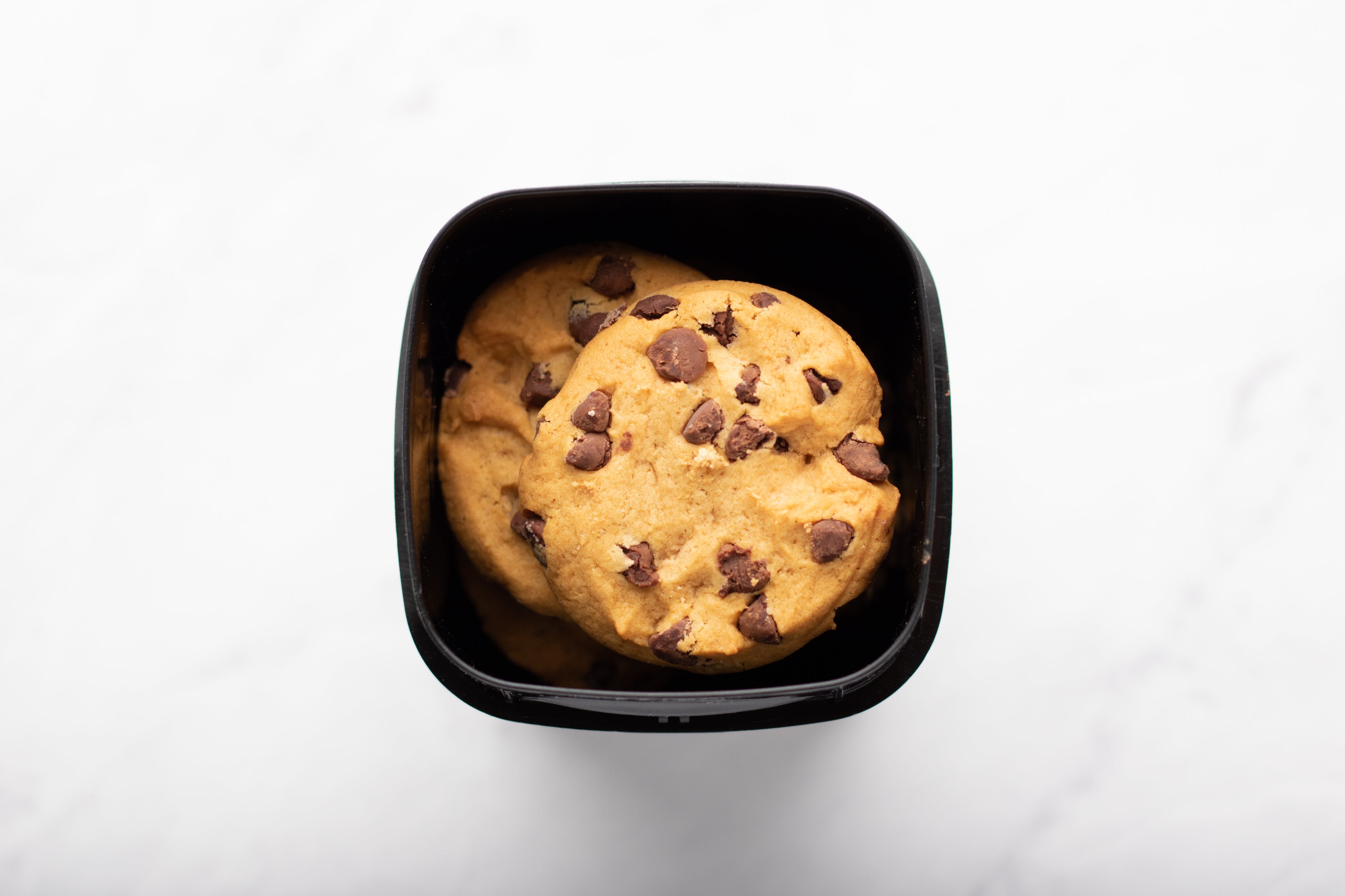 Two chocolate chip cookies in a black packaging container on a white background