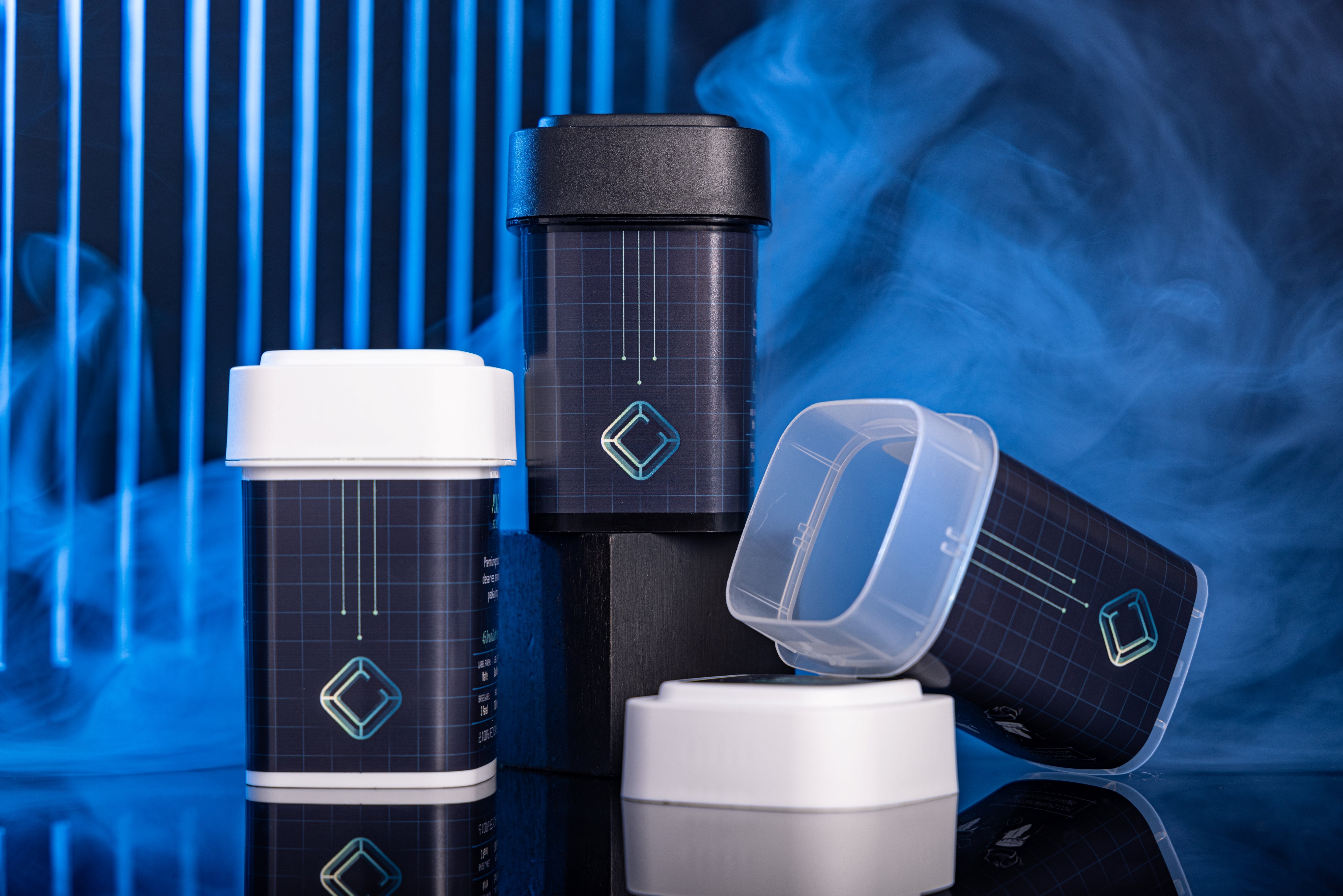 Set of black cannabis containers with white and clear lids on a reflective surface with blue background