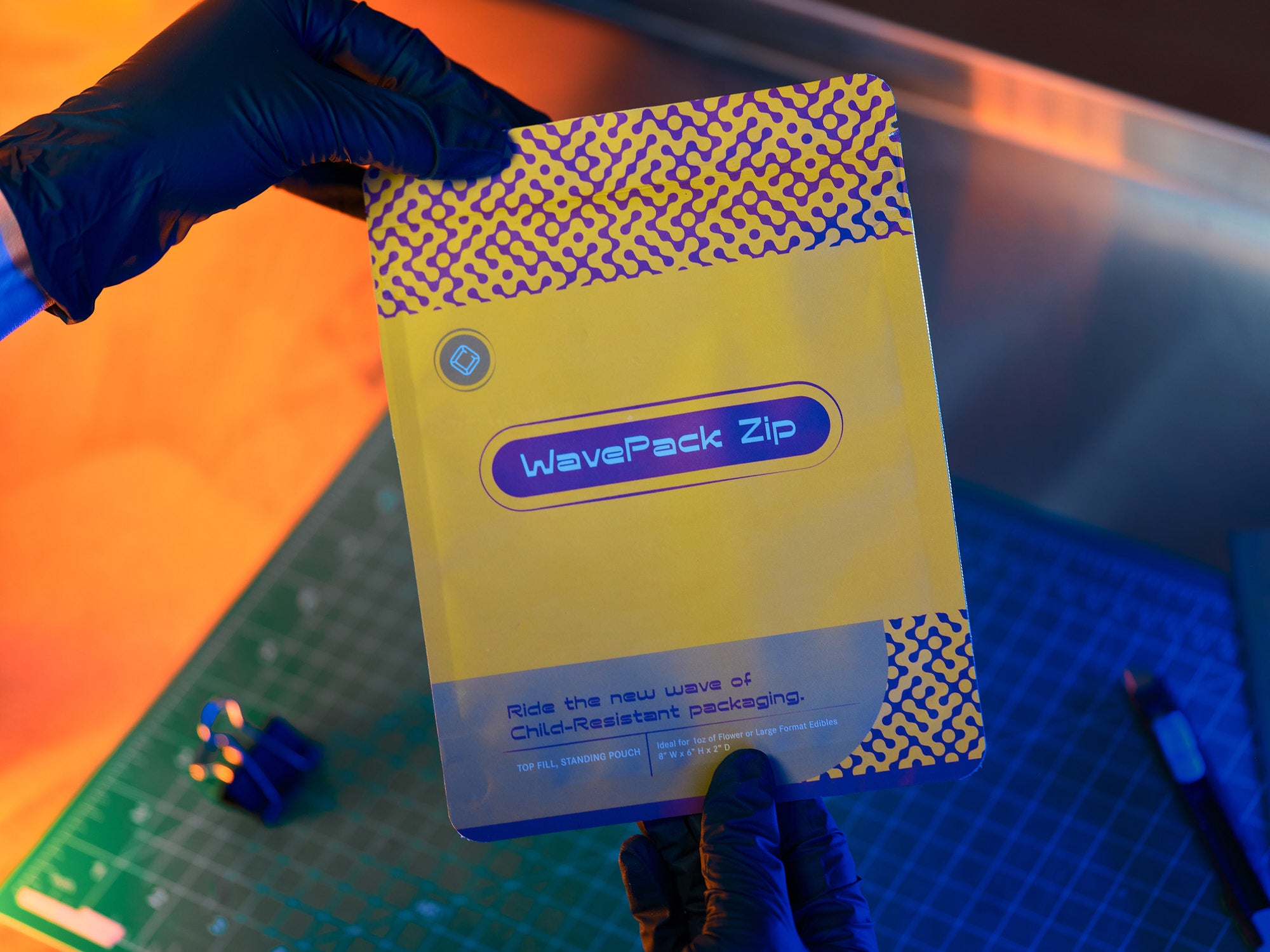 Yellow flexible cannabis packaging labeled 'WavePack Zip' is held by a gloved hand on a cutting mat.