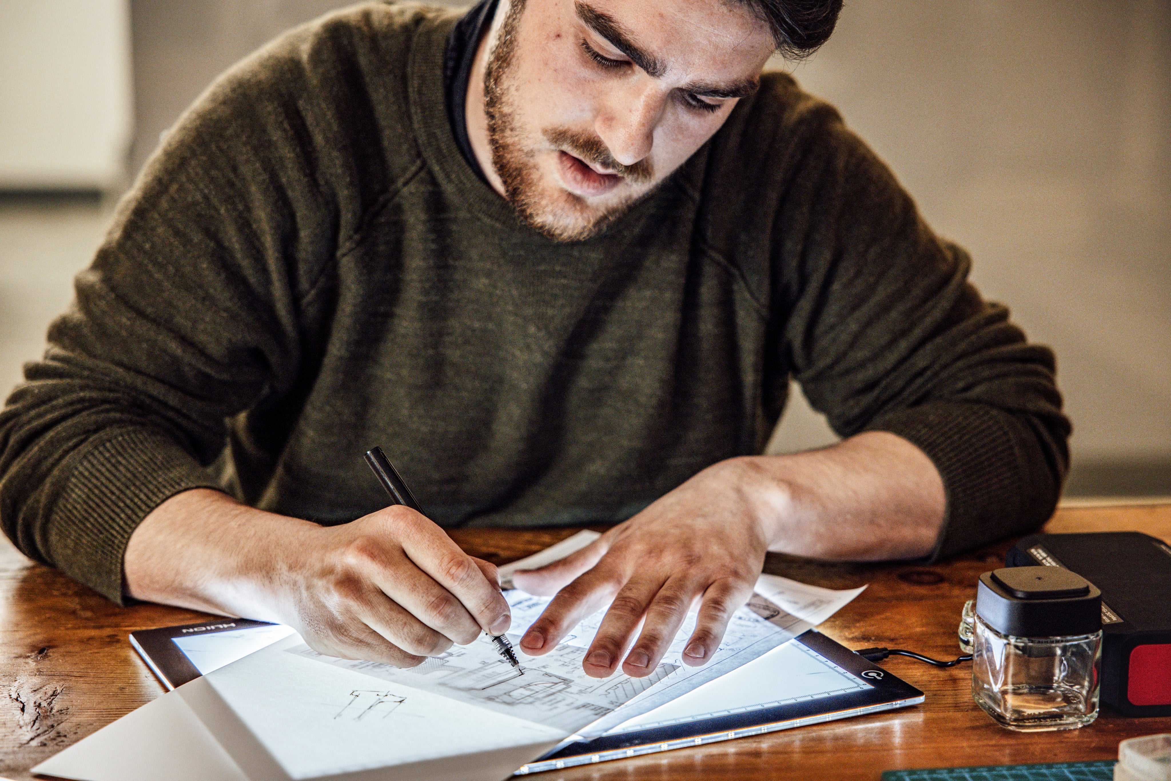 Man working on a drawing or design at a desk with a tablet and paper.