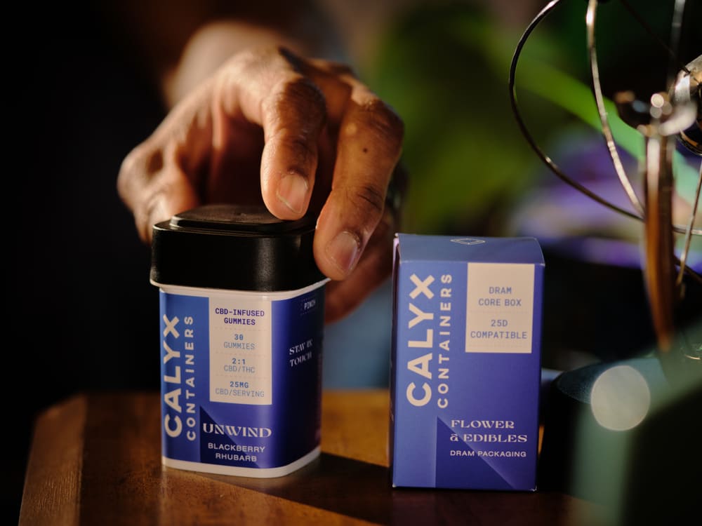 Hand holding a Calyx Containers product on a wooden surface with a blurred background