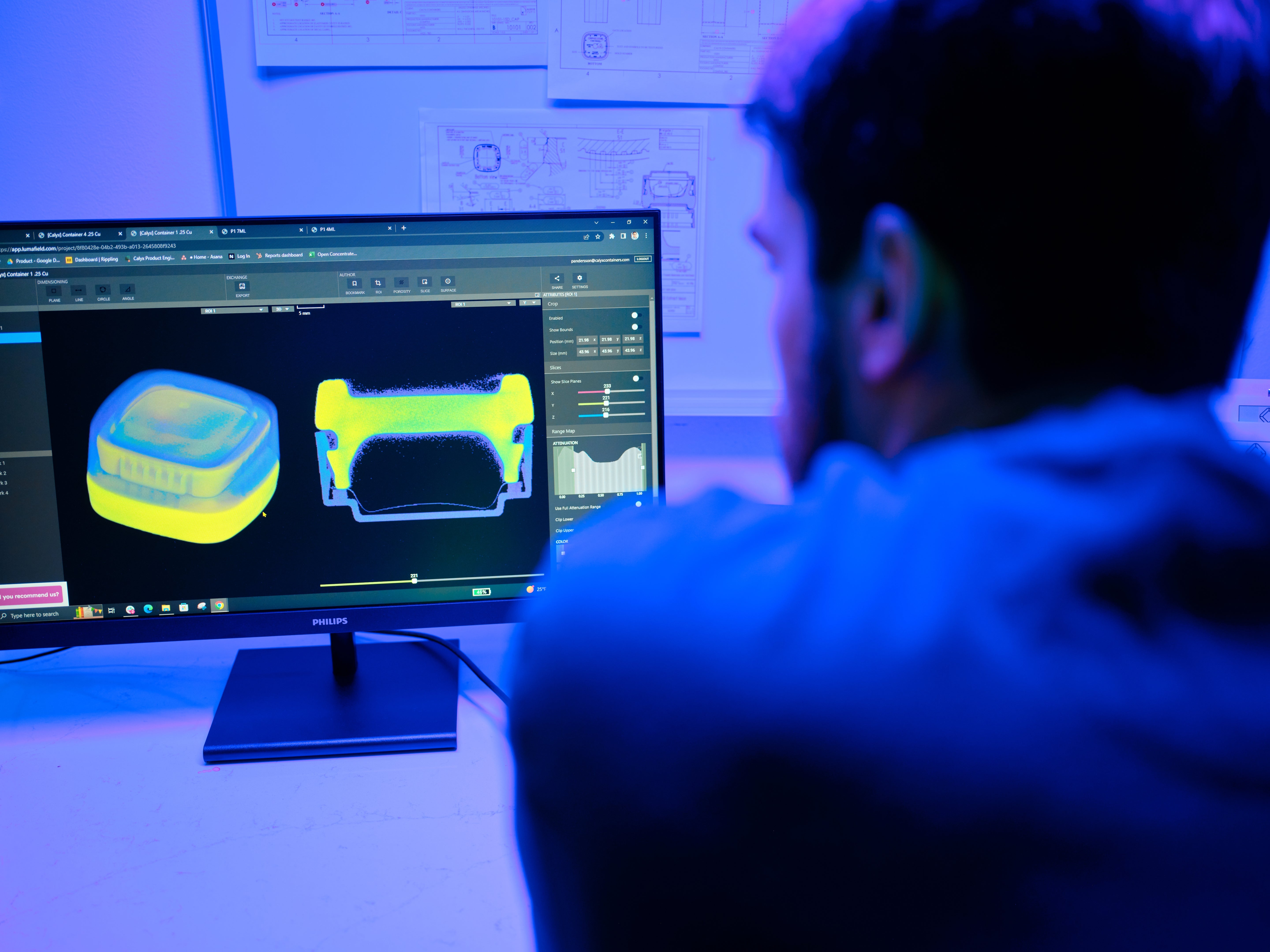 Person working on a computer with 3D modeling software in a blue-lit room.