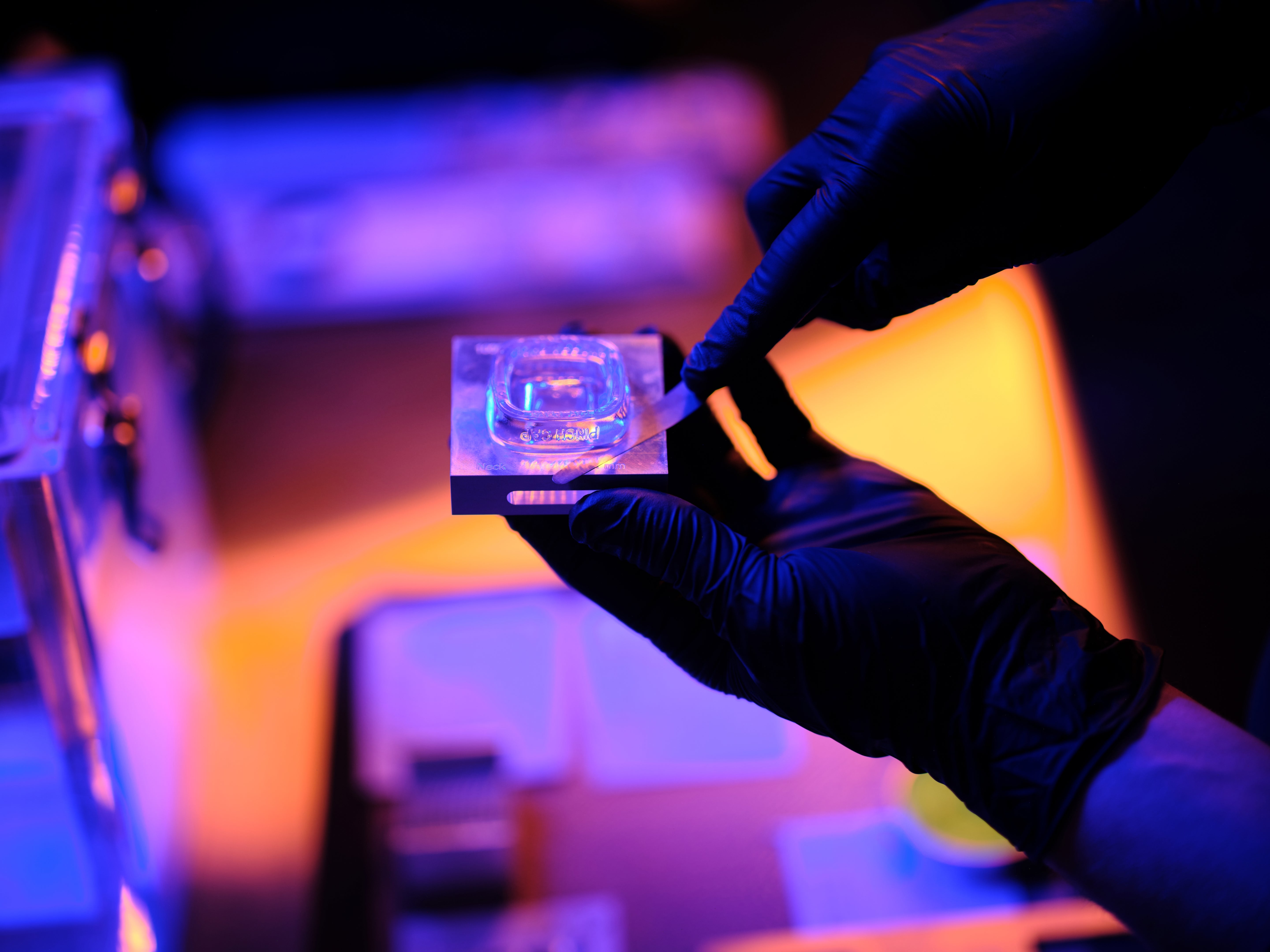 Person wearing gloves holding a marijuana concentrate container with a blue light inside, against a blurred background.