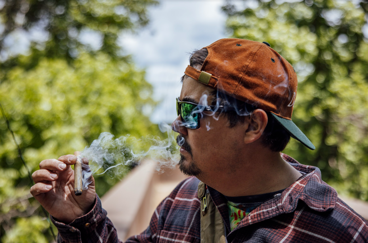 Man smoking large joint outdoors on a sunny day in the forest