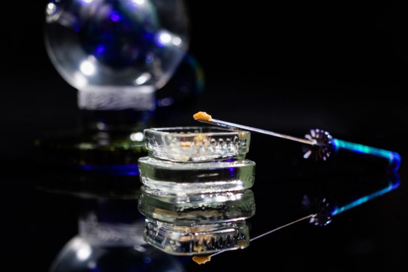 Cannabis concentrate on dabbing tool with rig in background