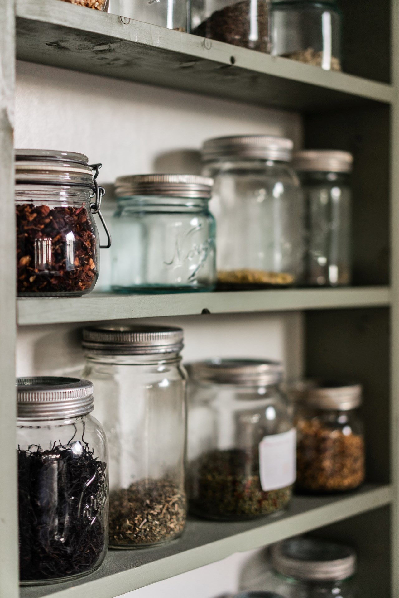 Collection of mason jars on shelves with a variety of dried teas and spices