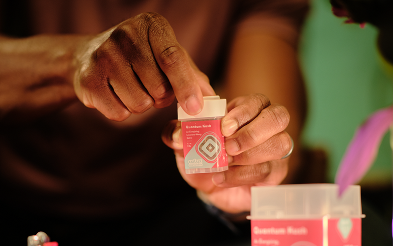 Person opening a Calyx dram with pink Quantum Kush branding